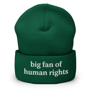 Puede incluir: Un gorro verde oscuro con la frase "big fan of human rights" bordada en blanco. El gorro, de estilo clásico, está diseñado para abrigar y expresar apoyo a los derechos humanos.