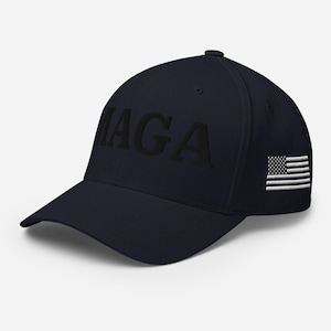 Könnte beinhalten: Eine marineblaue Baseballkappe mit dem Text "MAGA" in schwarzer Stickerei auf der Vorderseite. Auf der rechten Seite der Kappe ist eine weiß-graue amerikanische Flagge gestickt.