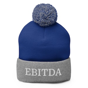 May include: A blue and grey knitted beanie with a white pom pom on top. The beanie has the word "EBITDA" embroidered on the cuff in white.