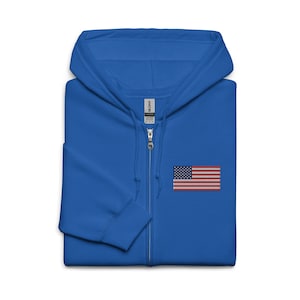May include: A royal blue zip-up hoodie with a small embroidered American flag on the chest. The hoodie features a hood, a full-length zipper, and a soft, comfortable fabric. The flag is red, white, and blue.