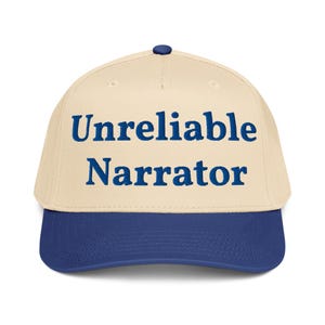 May include: A baseball cap with a cream-colored crown and a navy blue brim. The text "Unreliable Narrator" is embroidered in navy blue across the front of the cap. The cap has a curved brim and a button on top.