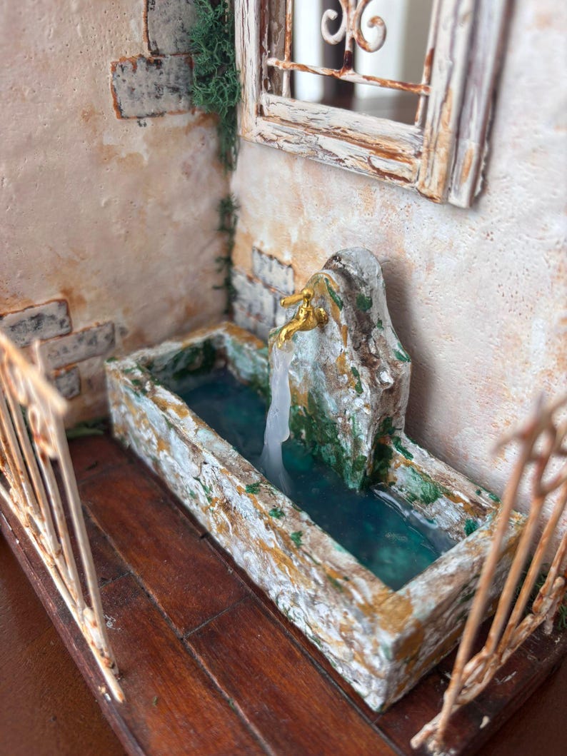May include: Miniature fountain with a stone basin and a golden faucet. The water is a clear blue, and the surrounding walls are textured with a weathered, aged appearance. The scene includes a small window and a decorative railing, evoking a rustic, old-world charm.
