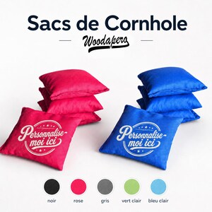 Könnte beinhalten: Pinke und blaue Cornhole-Säcke mit dem Text "Personnalise-moi ici" in Weiß. Das Bild zeigt auch Farboptionen: Schwarz, Rosa, Grau, Hellgrün und Hellblau. Die Säcke sind quadratisch und gestapelt.
