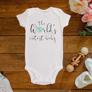 May include: White baby onesie with the text "the world's cutest baby" in black script with a small blue and green globe graphic.