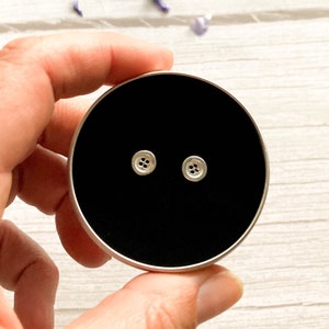 May include: A pair of silver button earrings in a black velvet box. The buttons have four holes.