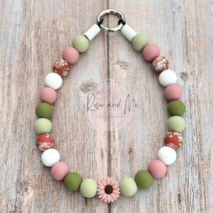 May include: A beaded dog collar with a variety of colorful beads in shades of pink, green, white, and floral patterns. The collar features a metal ring and a pink flower charm. The text "Rose and Me Pet Company" is visible.