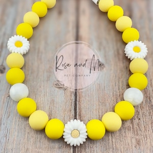 May include: A yellow and white silicone chew necklace for dogs with daisy flower charms. The necklace is made by Rose and Me Pet Company.