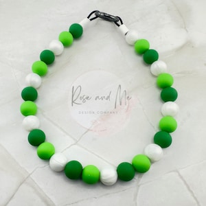 May include: A green, white, and green silicone bead necklace with a silver clasp. The beads are ombre, with a gradient of green to white to green.