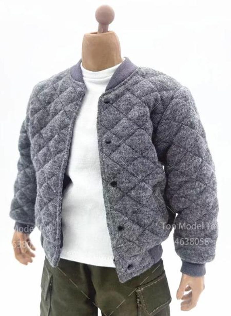 May include: A grey quilted bomber jacket with a diamond pattern, a ribbed collar, and black snap buttons. The jacket is worn over a plain white t-shirt. The outfit is completed with olive green cargo trousers featuring visible stitching and side pockets.