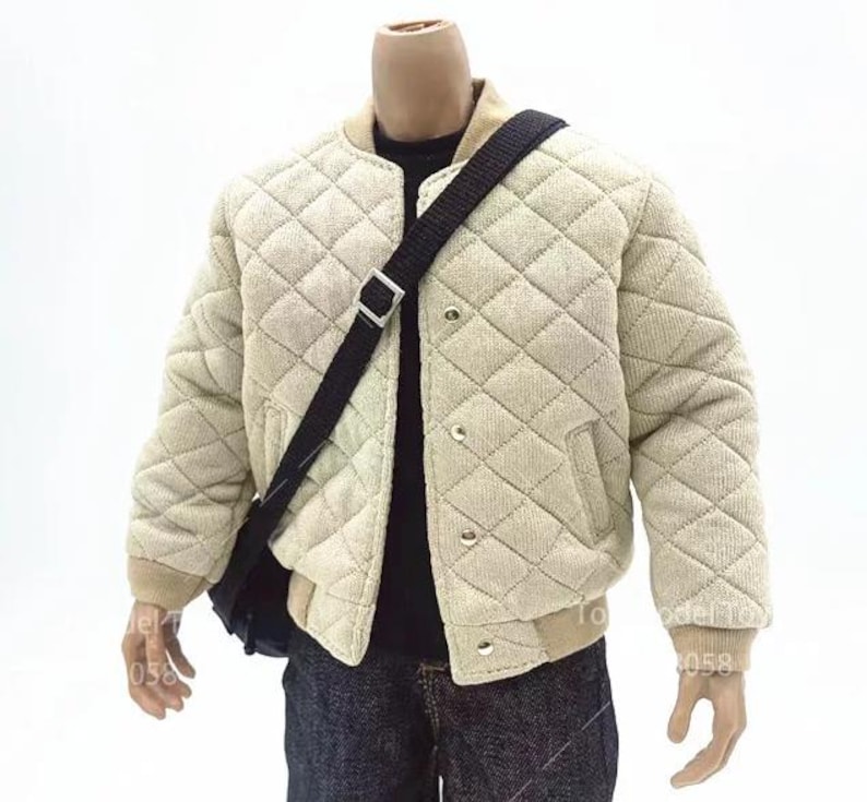 May include: A beige quilted bomber jacket with a ribbed collar and cuffs, featuring a front snap button closure and two side pockets. A black crossbody bag with a silver buckle strap is worn over the jacket, paired with a black shirt and dark jeans.