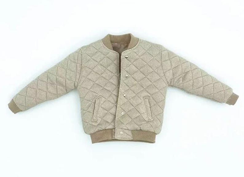 May include: A beige quilted bomber jacket featuring a diamond-stitched pattern, a ribbed collar, ribbed cuffs, and a ribbed hem. The jacket includes a front opening with visible silver-toned snap buttons and two vertical slit pockets on the front.