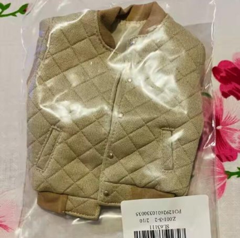 May include: A beige quilted bomber jacket with a textured fabric finish, a ribbed collar, and ribbed cuffs. The jacket features a front button closure with metallic buttons and two side pockets. It is enclosed in a clear plastic bag with a white label.