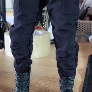 May include: Black cargo pants with multiple pockets and black combat boots. The pants have a slightly wrinkled appearance. The boots have a textured design and multiple straps.