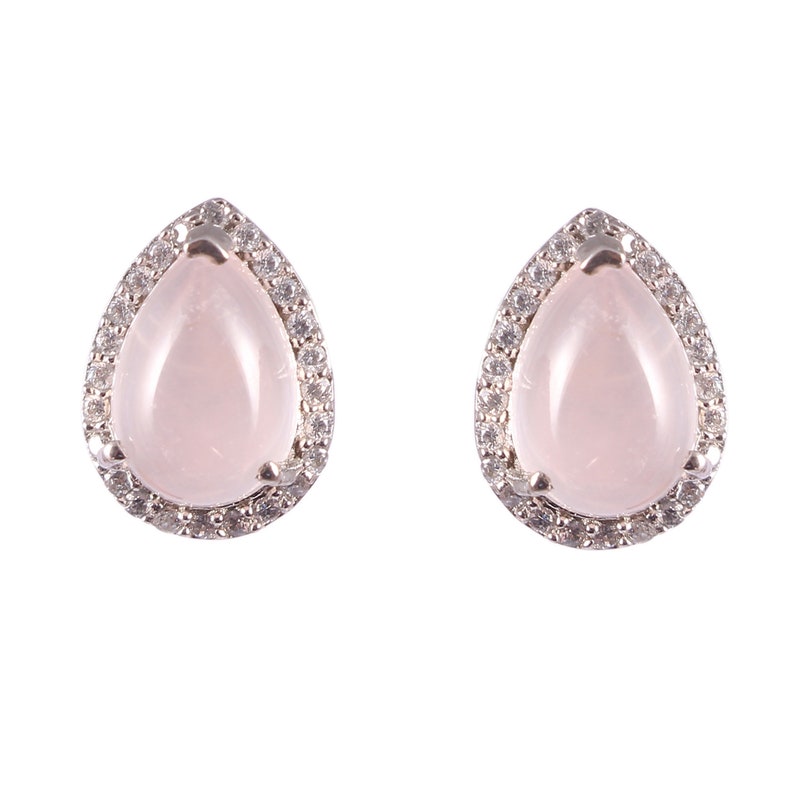 May include: A pair of teardrop-shaped stud earrings. Each earring features a pale pink gemstone center, surrounded by a halo of small, clear stones set in a silver-colored metal. The earrings are displayed against a white background.