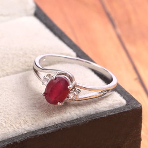 Può includere: Un anello d'argento con una pietra ovale rossa e pietre più piccole trasparenti sulla fascia.