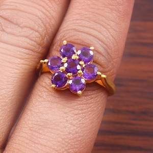 Peut inclure: Une bague en or avec un motif de fleur violette. La fleur est composée de sept pierres d'améthyste rondes.