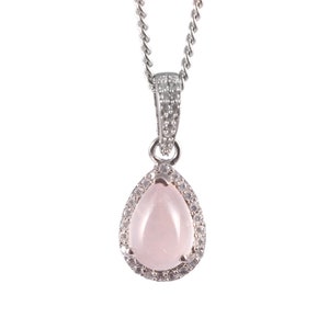 May include: A silver necklace with a pear-shaped pendant. The pendant features a light pink gemstone surrounded by small, clear stones. The chain is a delicate, twisted design.