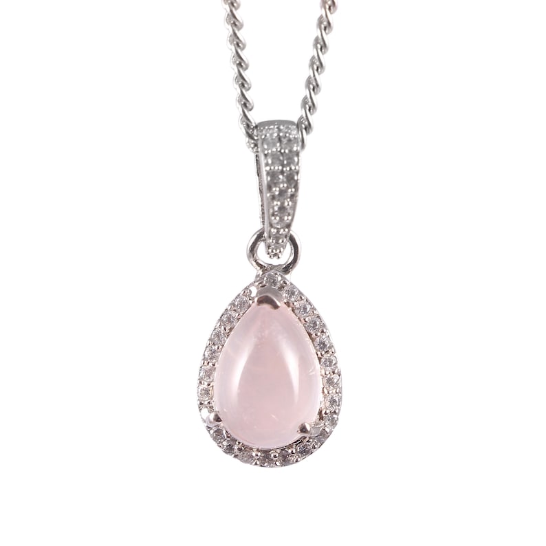 May include: A silver necklace with a pear-shaped pendant. The pendant features a light pink gemstone surrounded by small, clear stones. The chain is a delicate, twisted design.