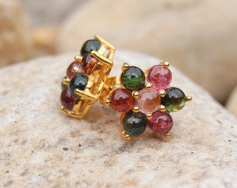 May include: A pair of gold earrings with a flower design. The earrings are set with multiple round, multi-colored gemstones.