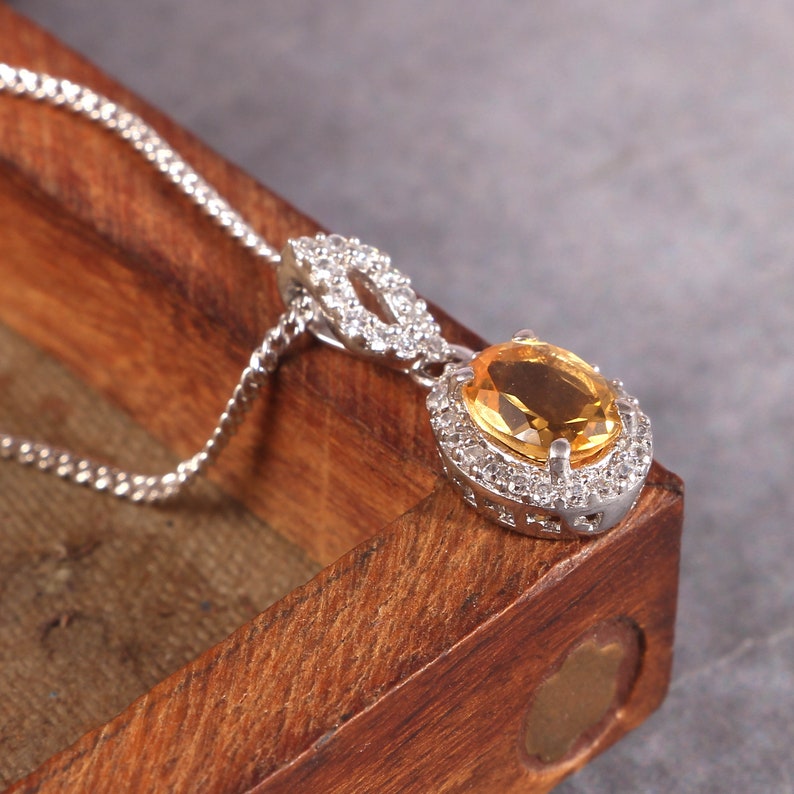 May include: A silver necklace with a pendant featuring a large, oval-shaped yellow gemstone surrounded by smaller clear gemstones.