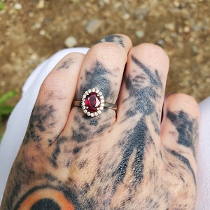 May include: A gold ring featuring a large oval ruby set within a halo of smaller diamonds.