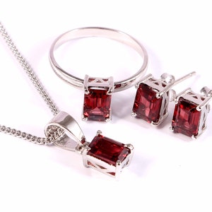 May include: A set of silver jewellery with red gemstone accents. The set includes a ring, a necklace, and a pair of earrings.