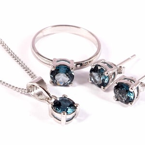 May include: A silver necklace, ring and earrings set with blue gemstones. The jewellery is made of sterling silver and features round, faceted stones.