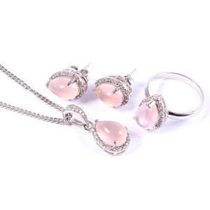 May include: A jewelry set featuring a necklace, earrings, and a ring. Each piece has a pear-shaped, light pink gemstone surrounded by a silver-colored metal setting with small, clear accent stones. The necklace has a delicate chain.
