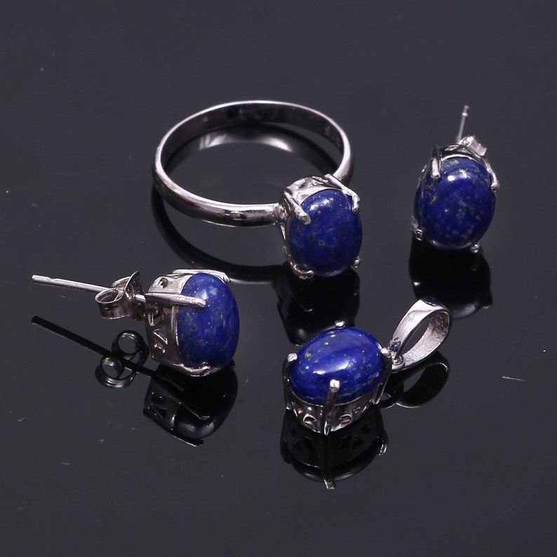 May include: A silver ring, earrings, and pendant necklace set with oval-shaped blue lapis lazuli stones.