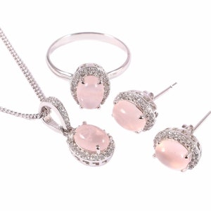 May include: A silver jewellery set with a pink oval gemstone pendant, ring and earrings. Each piece features a halo of smaller clear gemstones.