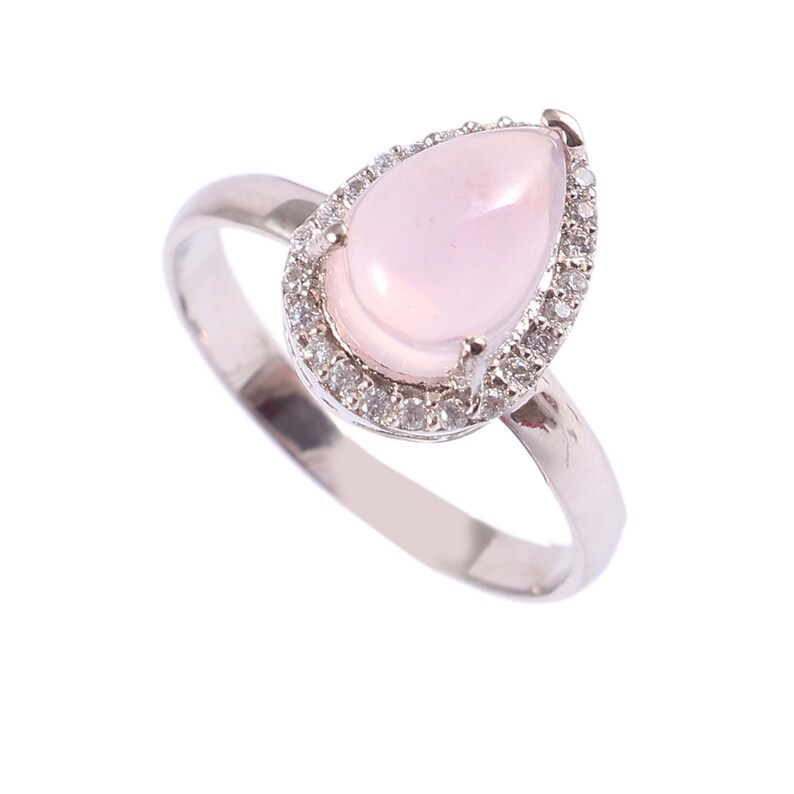 May include: A silver ring featuring a pear-shaped, light pink gemstone surrounded by a halo of small, clear stones. The ring's band is a simple, polished silver. The gemstone is the focal point of the ring.