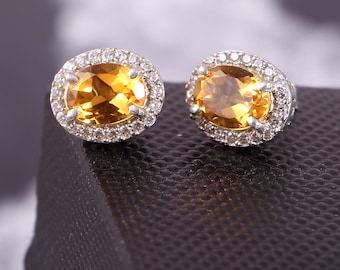 May include: A pair of silver earrings with a large oval-shaped topaz gemstone surrounded by a halo of smaller clear gemstones.