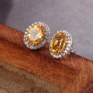 May include: A pair of oval-shaped earrings with a yellow gemstone surrounded by a halo of smaller white gemstones.