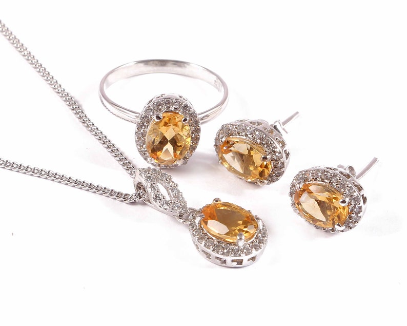 May include: A set of silver jewelry with a yellow topaz gemstone. The set includes a ring, a necklace, and a pair of earrings.
