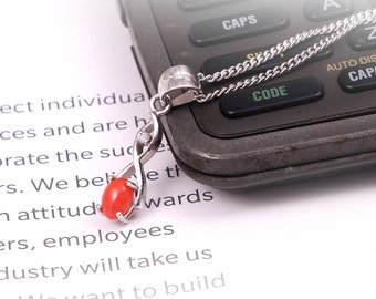 May include: A silver necklace with a red coral pendant and a small diamond accent. The necklace is lying on a white surface with text about business and success.
