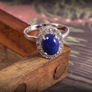 Puede incluir: Un anillo de plata con una gran piedra ovalada de lapisl&aacute;zuli azul rodeada de piedras m&aacute;s peque&ntilde;as de circonita c&uacute;bica transparentes.