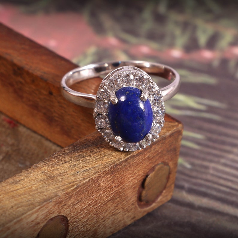 Puede incluir: Un anillo de plata con una gran piedra ovalada de lapisl&aacute;zuli azul rodeada de piedras m&aacute;s peque&ntilde;as de circonita c&uacute;bica transparentes.