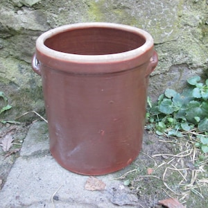 Könnte beinhalten: Ein brauner Keramiktopf mit zwei Metallgriffen. Der Topf steht auf einer Steinoberfläche.