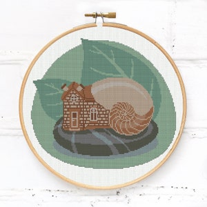 Op de afbeelding: Kruissteekpatroon van een slak met een huis op zijn rug, zittend op een rots met een groen blad erachter.