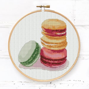May include: A stack of four colorful macarons with pink, yellow, and white frosting. A green and white macaron is to the left of the stack.