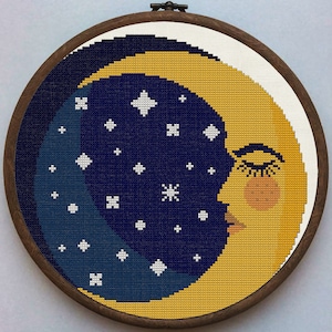 Peut inclure: Une lune en croissant jaune avec un visage endormi et des cils, entourée d'étoiles blanches sur un fond bleu foncé. La lune est brodée sur une toile ronde avec un cadre en bois.