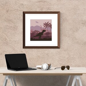 May include: A framed print of a dinosaur silhouette in a pink and purple landscape with palm trees. The print is hanging on a beige wall above a wooden desk with a laptop, headphones, and sunglasses.