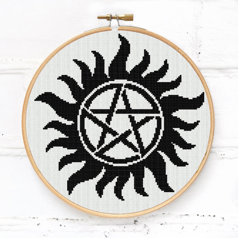 May include: Black and white embroidery hoop with a pentagram inside a sun symbol.