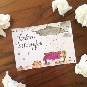 Könnte beinhalten: Eine handgezeichnete Illustration einer Person, die auf einer Bank unter einer grauen Regenwolke schläft. Der Text "Seelen-schnupfen" ist in schwarzer Kursivschrift auf weißem Hintergrund geschrieben. Die Illustration ist von einer braunen Holzoberfläche umgeben.