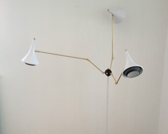 Może przedstawiać: Biała lampa stojąca z trzema regulowanymi ramionami i białymi kloszami. Lampa ma czarną podstawę i złotą metalową ramę.
