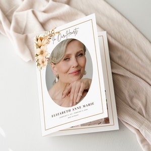 Pode incluir: Um cartão de memória com uma foto de uma mulher dentro de uma moldura oval, rodeada por detalhes florais. O texto "In Our Hearts" está no topo, com o nome "ELIZABETH ANNE MARIE" e as datas abaixo. O cartão tem uma borda dourada.