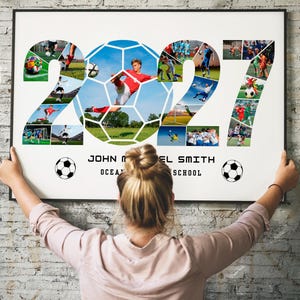 May include: A rectangular wall poster featuring a photo collage arranged in the shape of the number 2027, with a soccer ball graphic in the center. The text reads JOHN MICHAEL SMITH and OCEAN SCHOOL, flanked by two small black and white soccer ball icons.