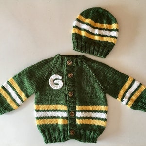 May include: A green knitted cardigan with yellow and white stripes and a felt 'G' on the front. It has a matching green knitted hat with yellow and white stripes.