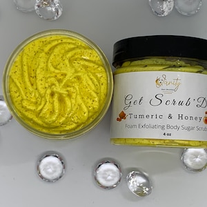 May include: A 4 ounce jar of yellow turmeric and honey body scrub. The jar is labelled "Get Scrub'D Turmeric & Honey Foam Exfoliating Body Sugar Scrub".
