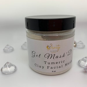 May include: A white jar with a black lid containing a light brown powder. The label reads "Get Mask' D Turmeric Clay Facial Mask 4 oz".
